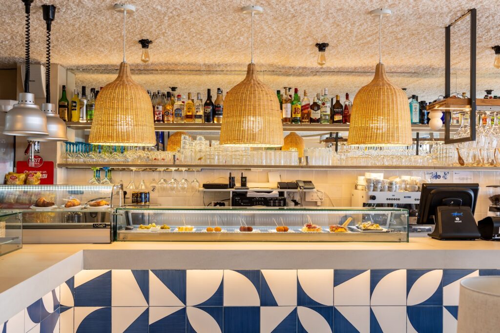 Vista del interior de un bar o restaurante con decoración en tonos azules y blancos, y una variedad de bebidas en las estanterías.