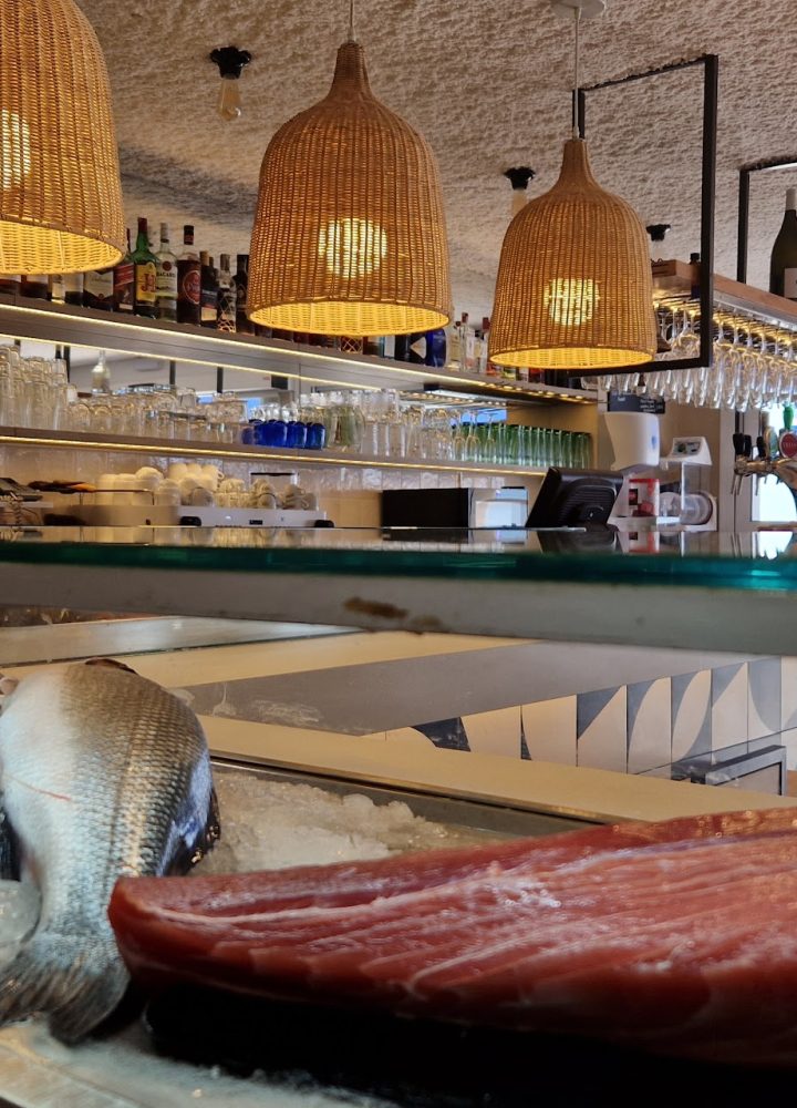 Interior de un restaurante con lámparas colgantes de mimbre y una vitrina de pescado fresco en primer plano.